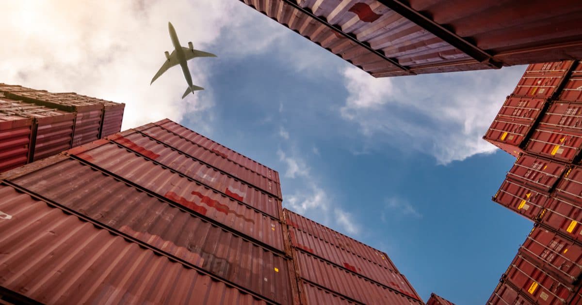 Stacked shipping containers seen from below with a cargo aircraft passing overhead